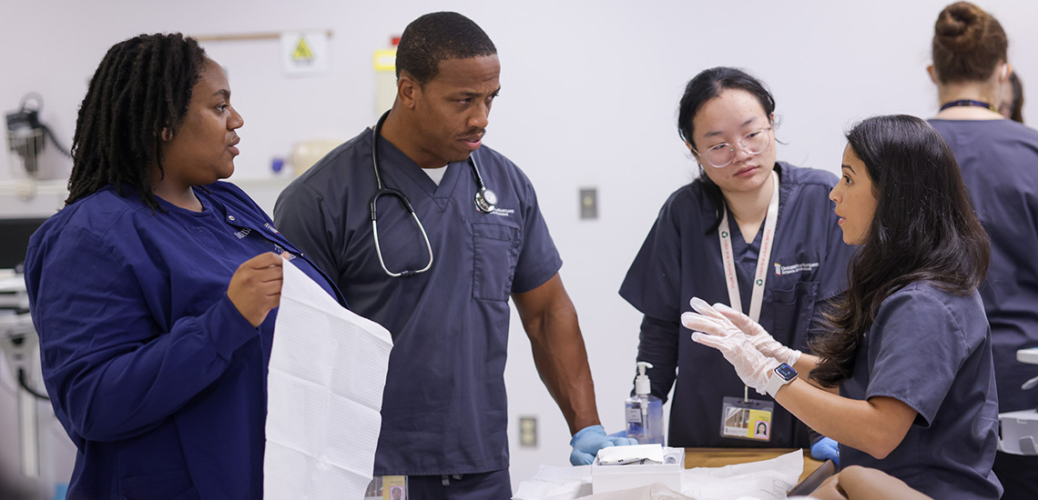 Three nursing students chat with an instructor in the sim lab