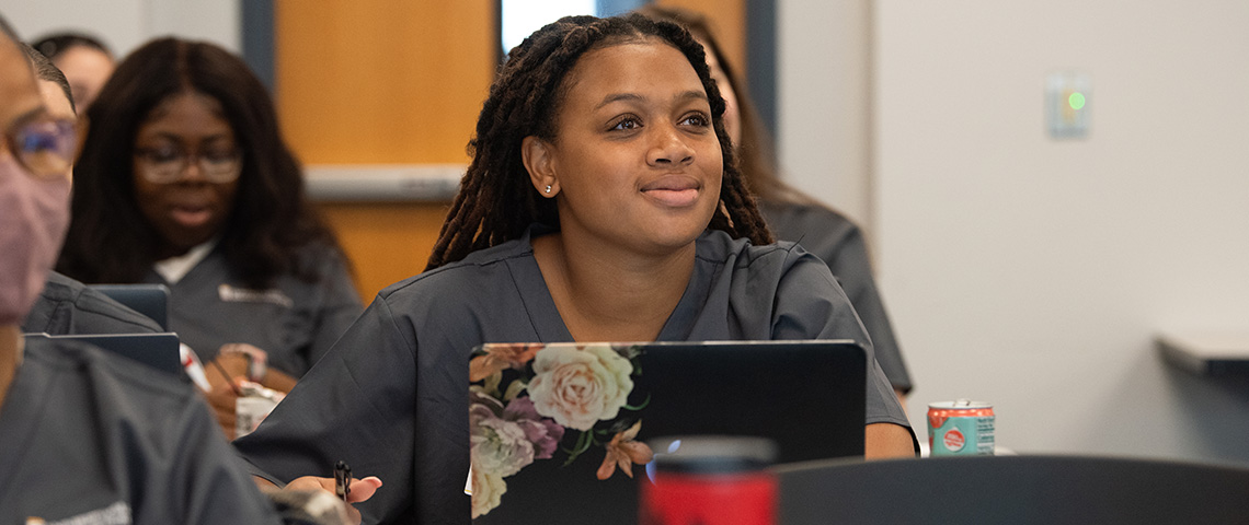 A woman in scrubs looks up the front of the classroom