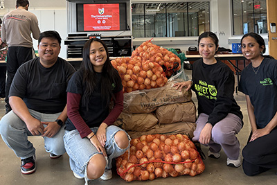 Four nursing students kneel on either side of a large pile of onions in red mesh bags